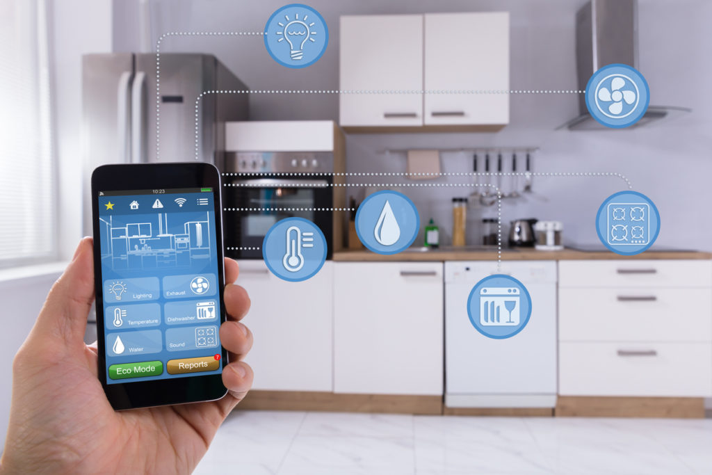 Pertsona baten eskuaren lehen planoa Smart Home aplikazioa erabiliz sukaldean telefonoan